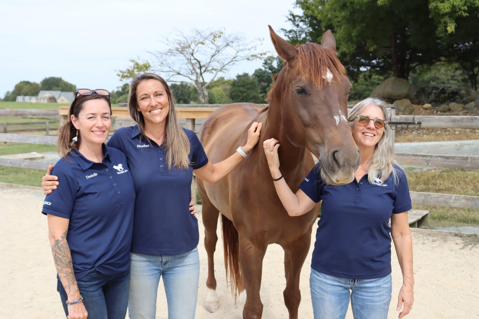 Three women in matching navy shirts standing with a chestnut horse
